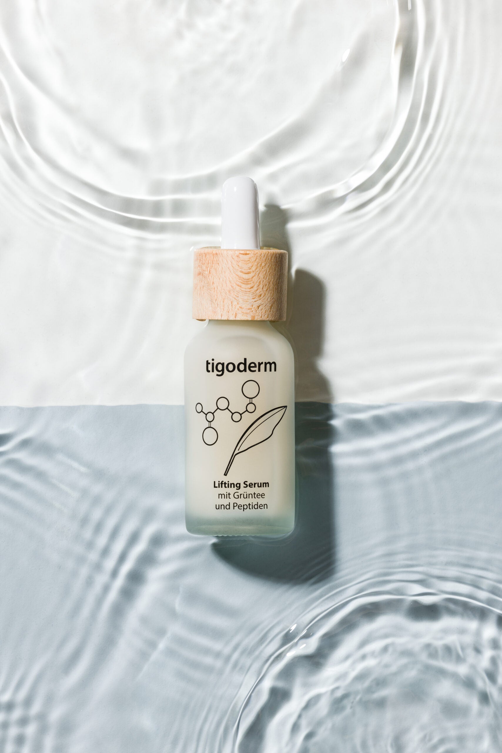 tigoderm Anti-Aging Lifting Serum mit EGCG & Peptiden in Pipettenflasche auf Wasserwellen, vegane Naturkosmetik.