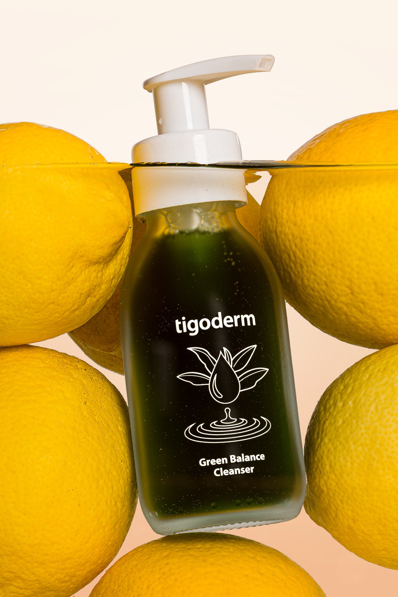 tigoderm Green Balance Cleanser im Glasflakon mit Spender, umgeben von Zitronen in Wasser zur Gesichtsreinigung.