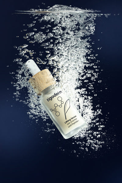 tigoderm Anti-Aging Lifting Serum mit EGCG & Peptiden in Unterwasser-Szene mit Luftblasen vor blauem Hintergrund.