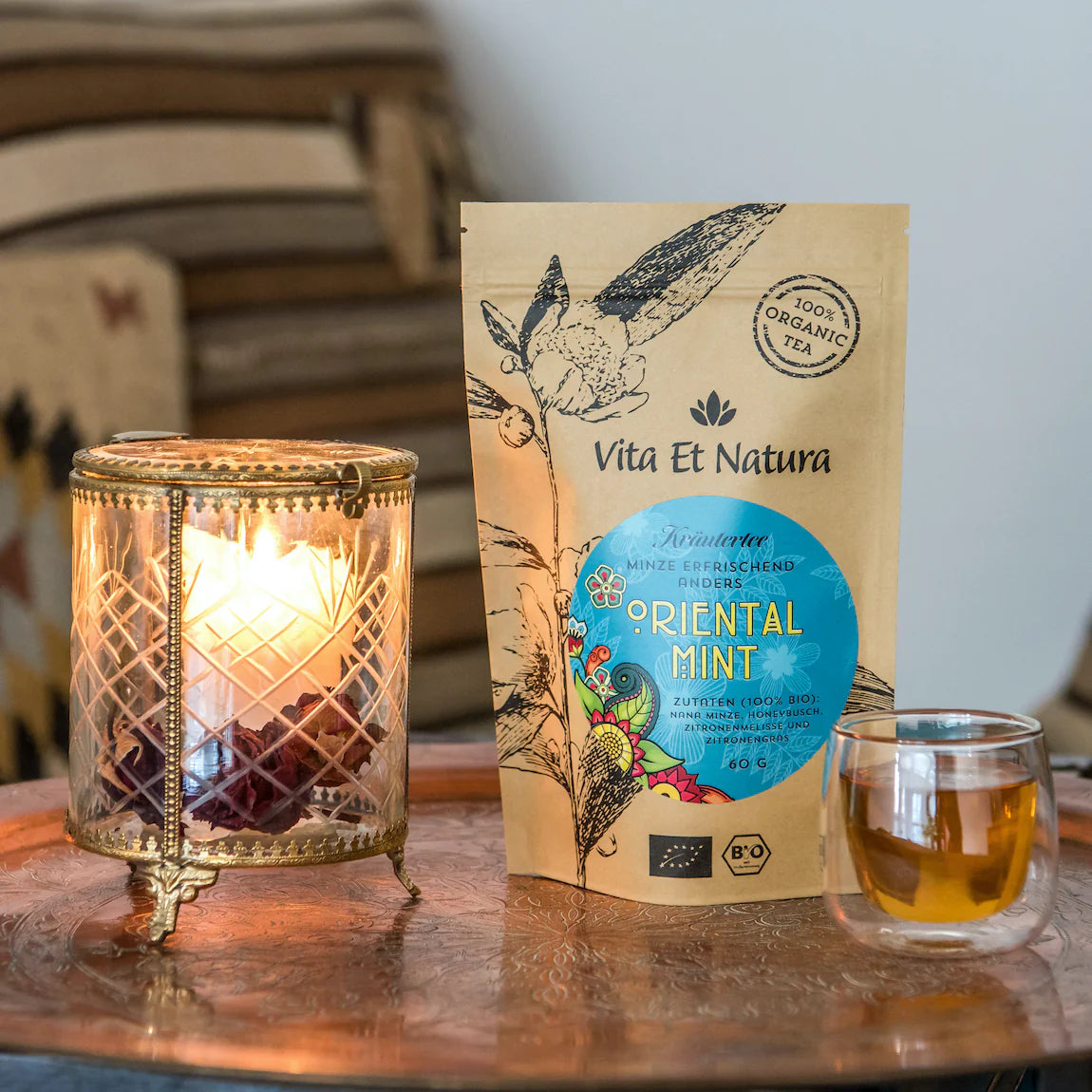 Orientalischer Bio-Minztee Nana Minze von Vita Et Natura neben einer Laterne und einem Teeglas auf einem Kupfertablett.